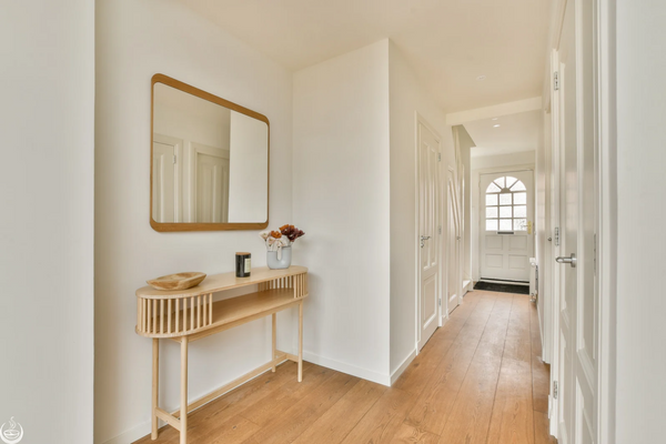 A bright hallway with a wooden console table, leading to a front door with a window