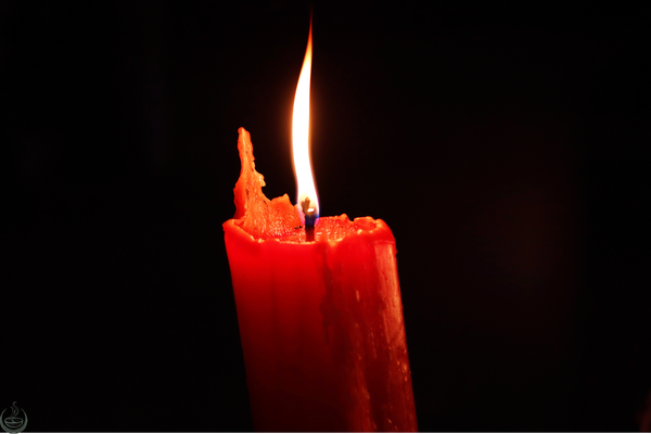 Red candle with melted wax burning with a single tall flame against a black background