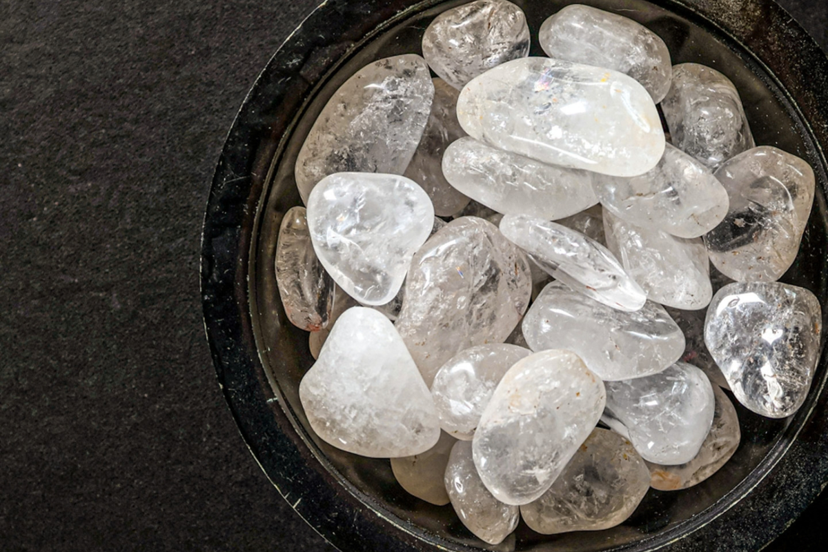 A black bowl of clear quartz tumbled stones on a black surface