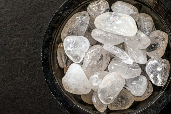 A black bowl of clear quartz tumbled stones on a black surface