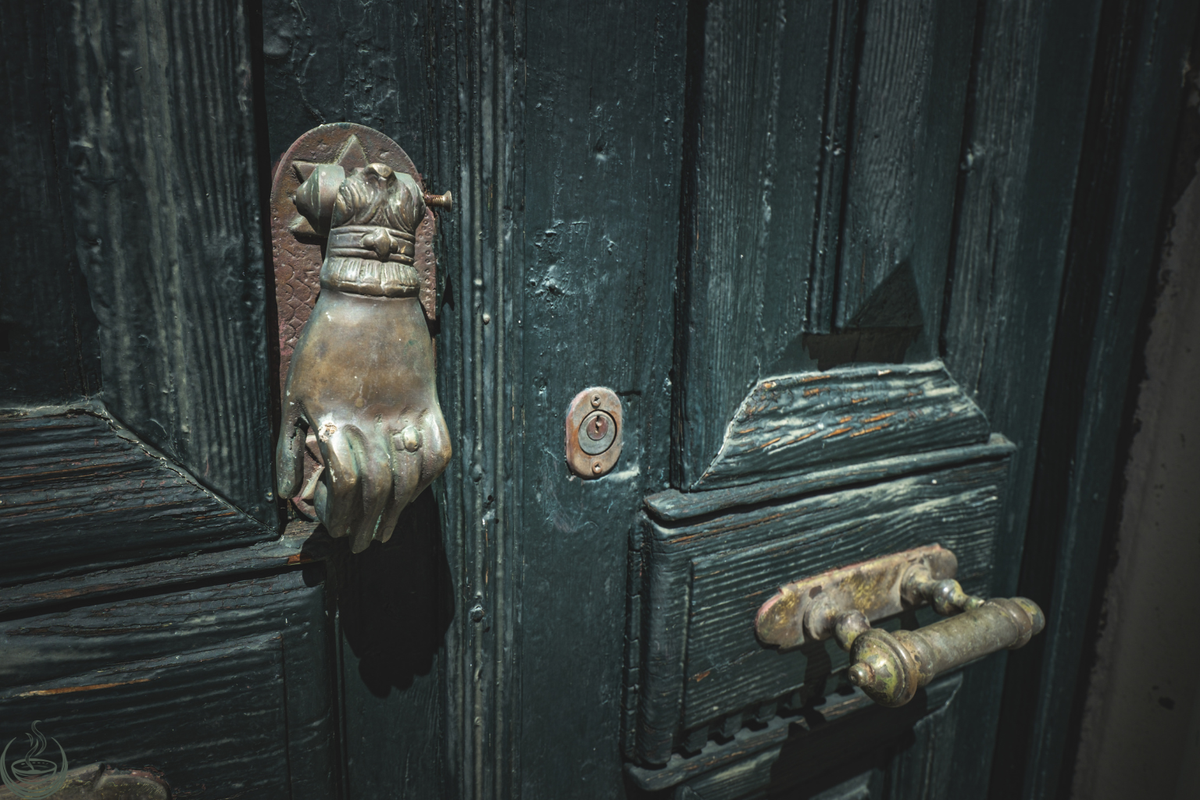A brass hand-shaped door knocker on a weathered dark green door