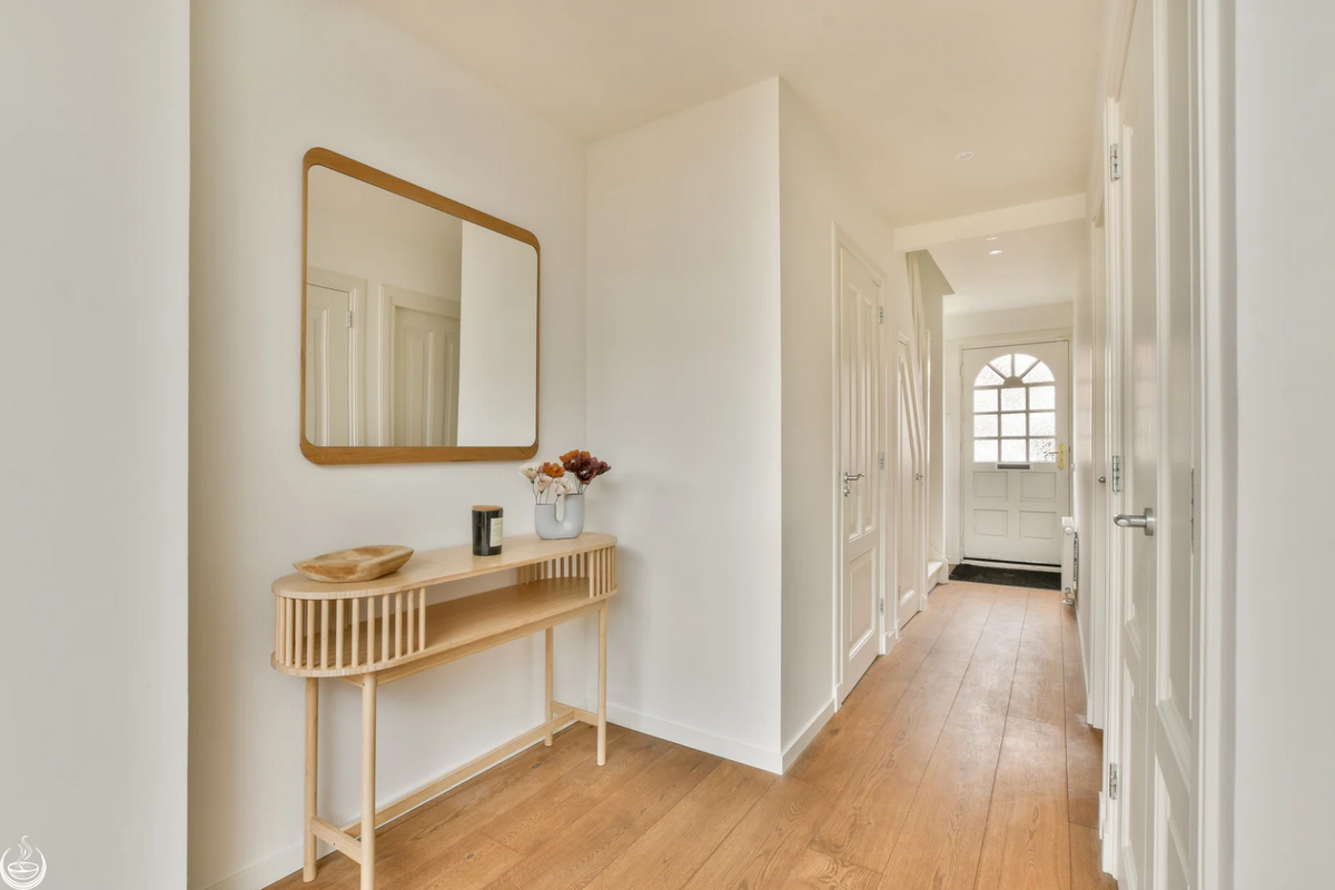 A bright hallway with a wooden console table, leading to a front door with a window
