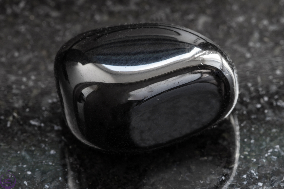 A polished black onyx tumbled stone on a dark speckled surface
