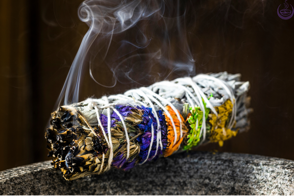 A smoldering smudge bundle wrapped with dried flowers, smoke rising against a dark background