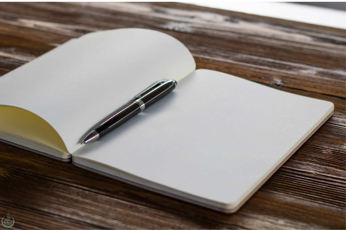 An open blank notebook with a black pen resting on it, on a dark wooden table