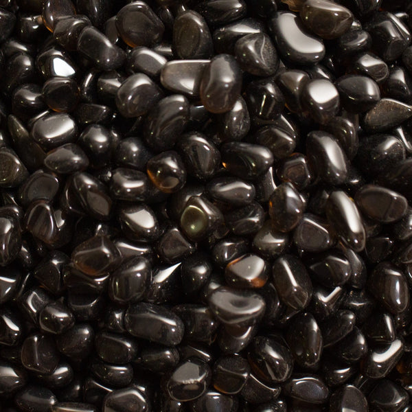 Small, smooth, translucent black Apache Tears stones with a glassy surface, some catching light at the edges.
