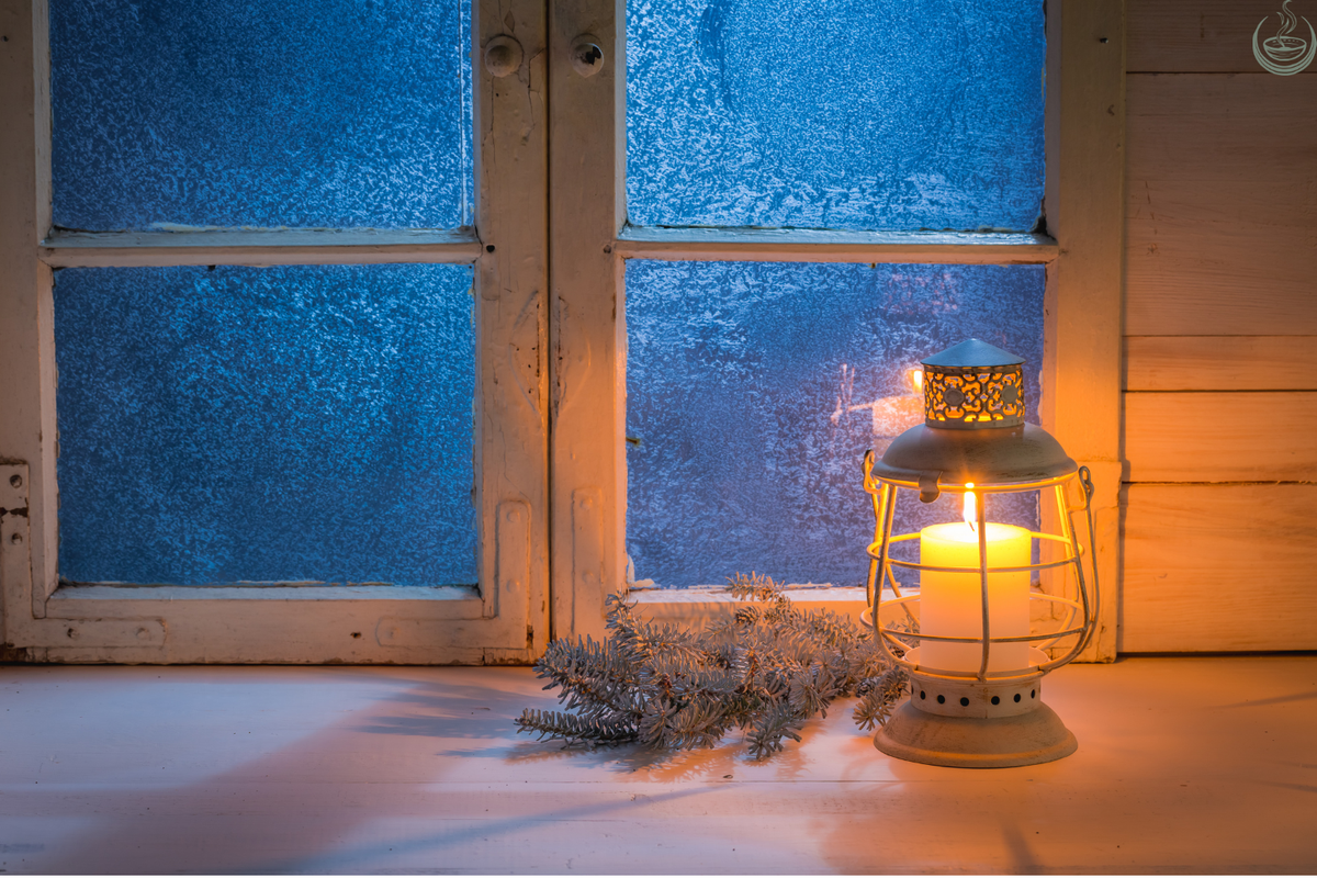 Candle glowing inside a lantern on a frosted windowsill in winter, with a sprig of fir beside it