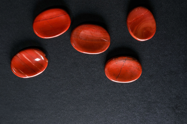 Five red jasper worry stones on a black surface