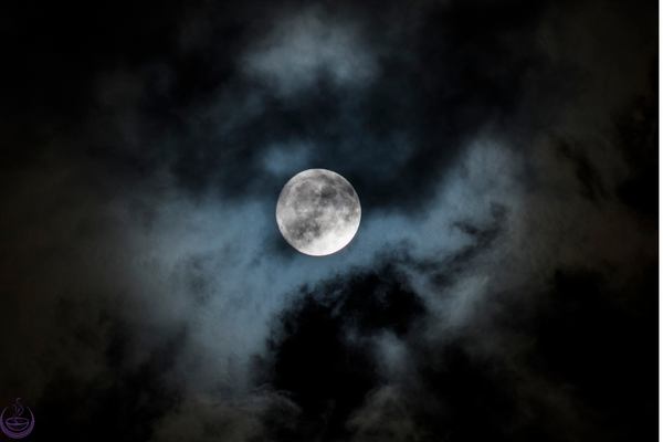 Full moon glowing through dark clouds at night