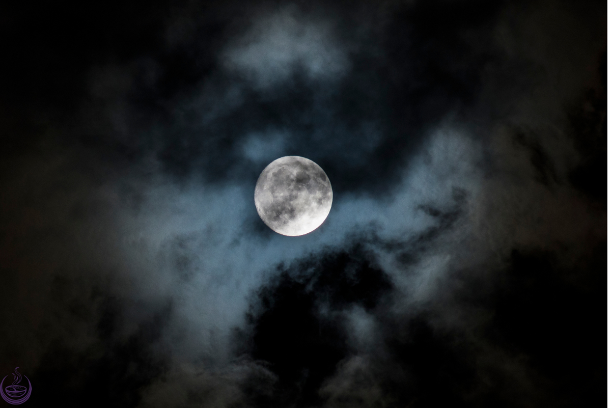 Full moon glowing through dark clouds at night
