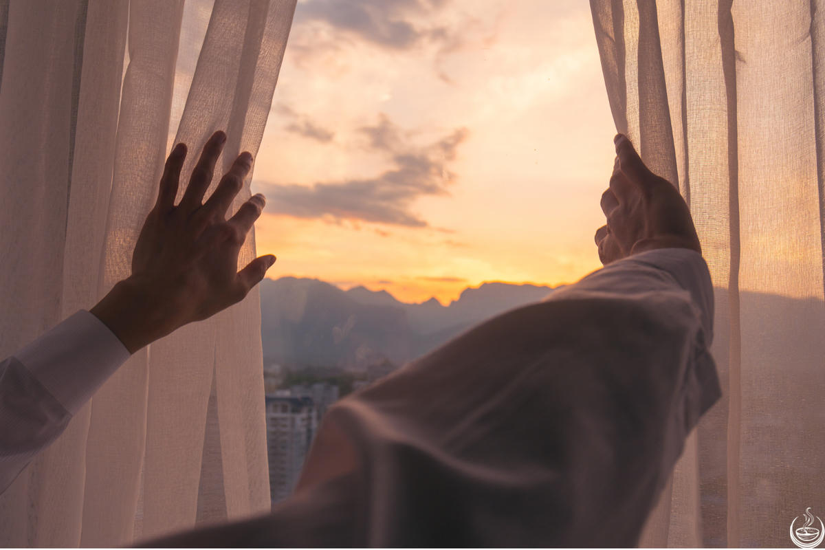 Hands drawing sheer curtains apart to a sunrise over distant hills