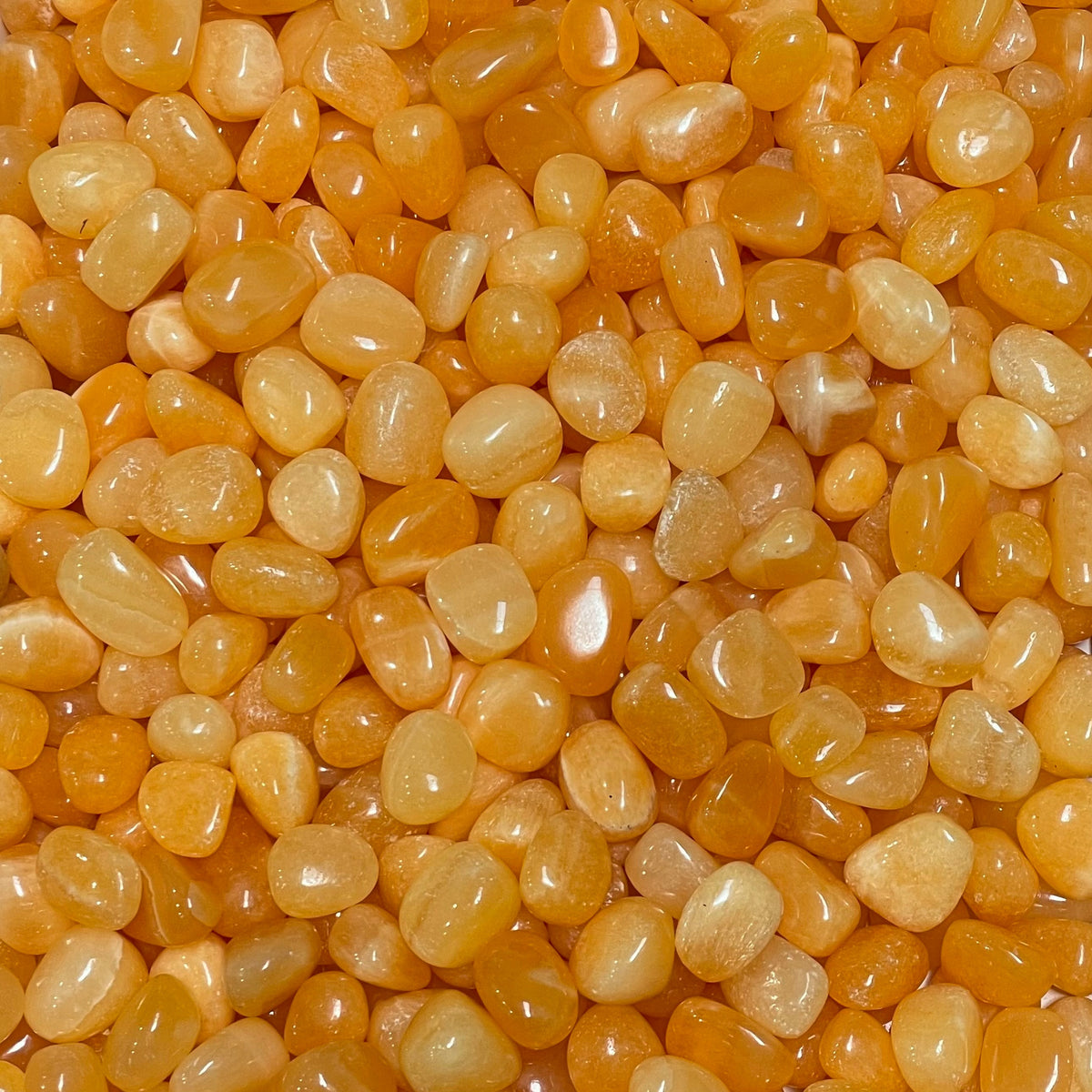 Tumbled orange calcite stone with a warm honey-to-amber glow, soft translucency, and faint natural banding