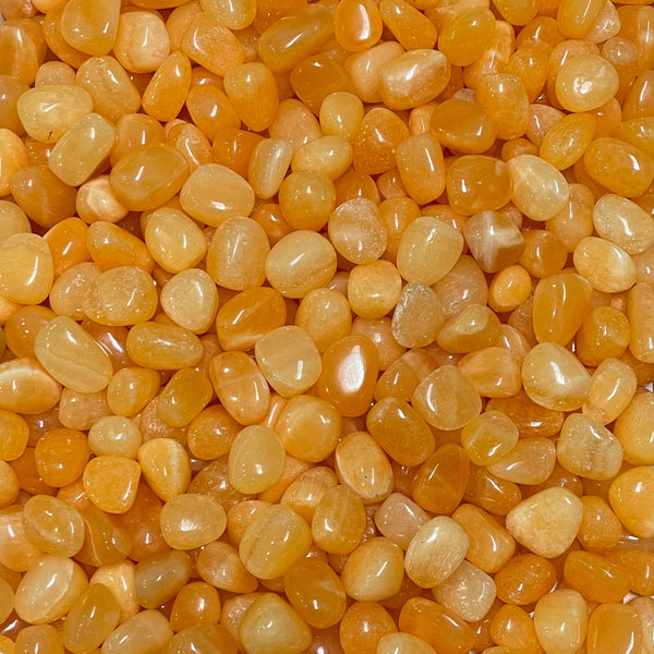 Tumbled orange calcite stone with a warm honey-to-amber glow, soft translucency, and faint natural banding