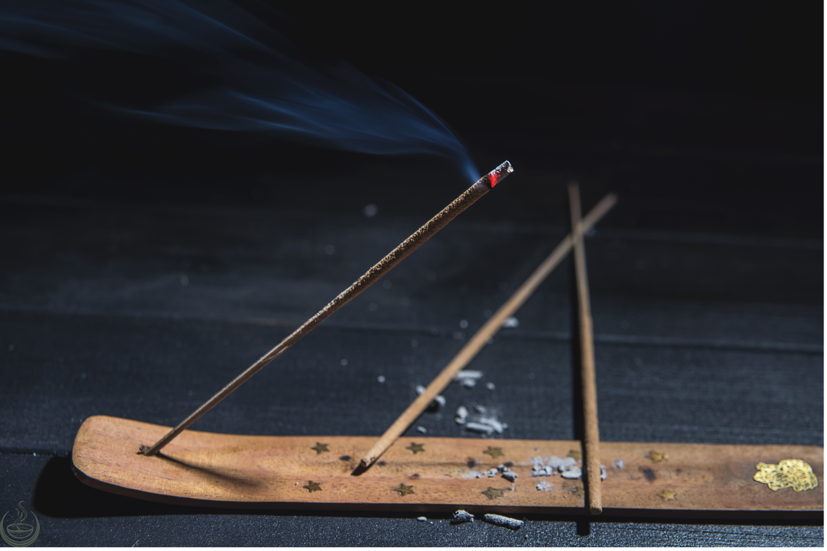 Lit incense stick with smoke rising from a wooden holder
