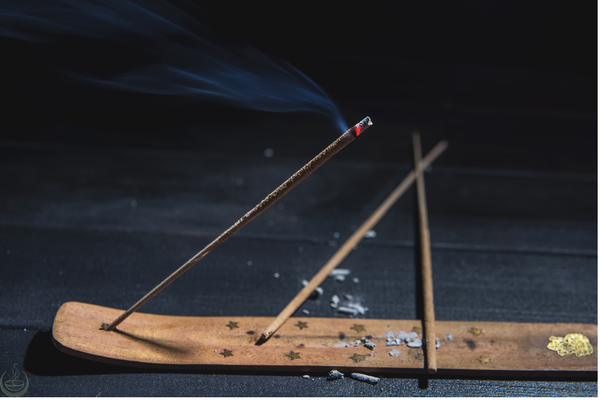 Lit incense stick with smoke rising from a wooden holder