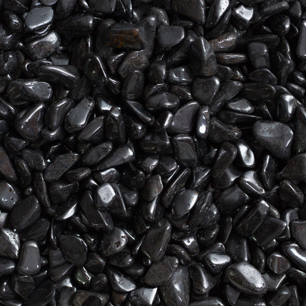 A dark, metallic-black magnetite specimen with a rough, angular octahedral surface, shown attracting small iron filings or a paperclip to demonstrate its natural magnetism.