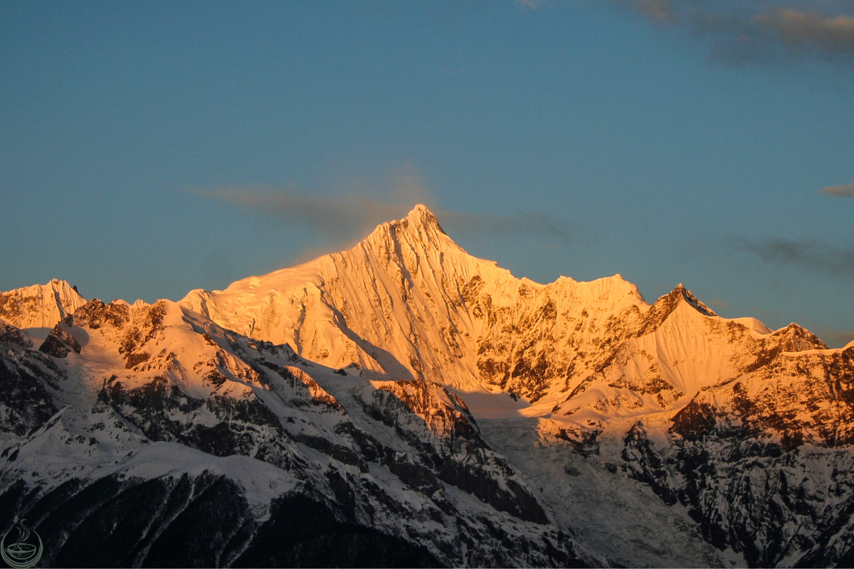 Snow-covered mountain peak lit gold by the first light against a deep blue sky
