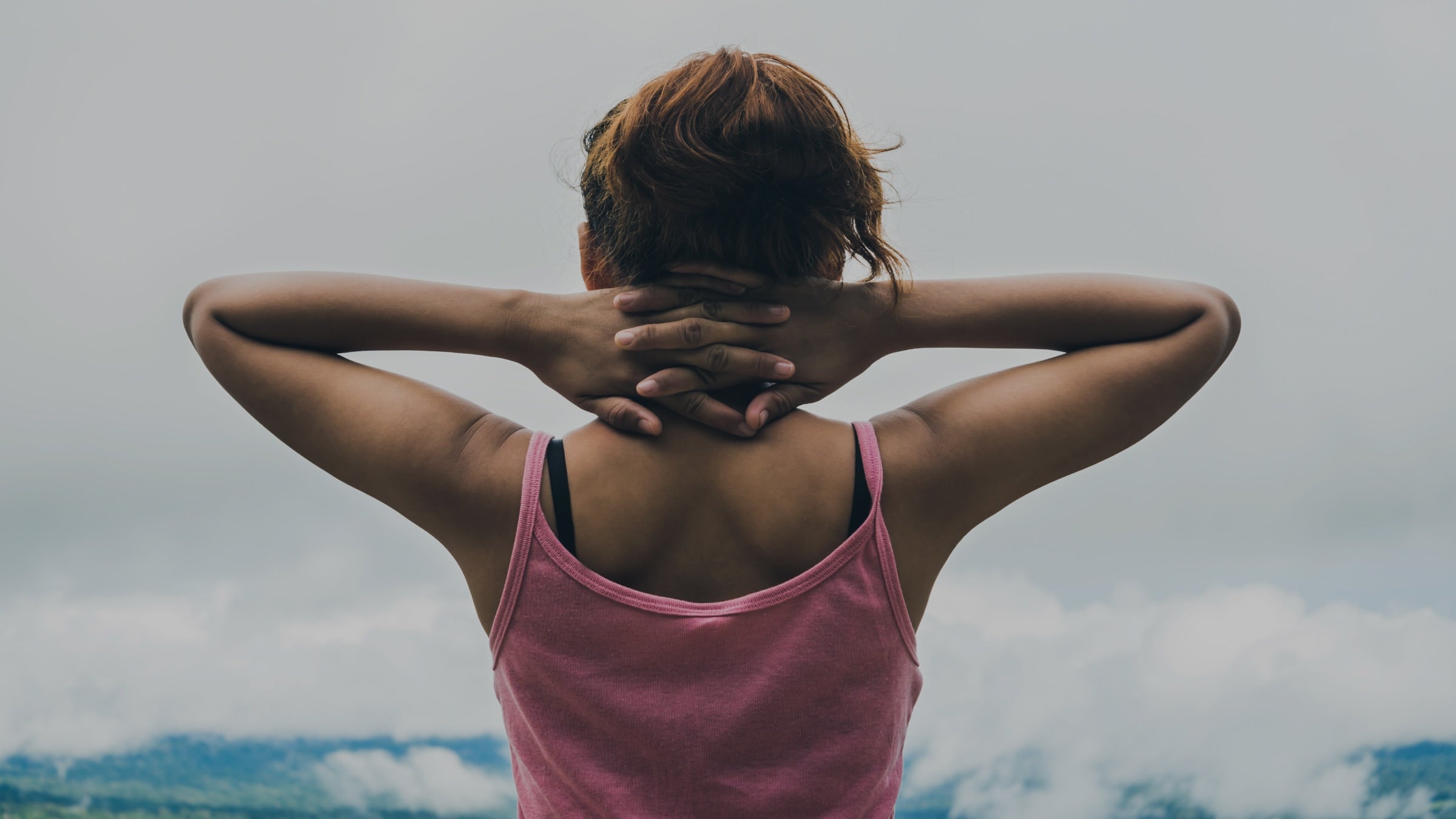 Person wearing a pink tank top with a cloudy sky background