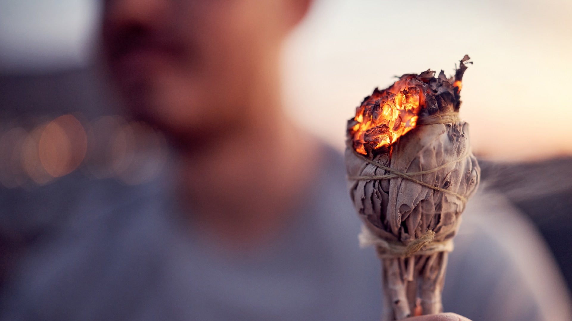 Person holding a smoldering sage bundle with a blurred background