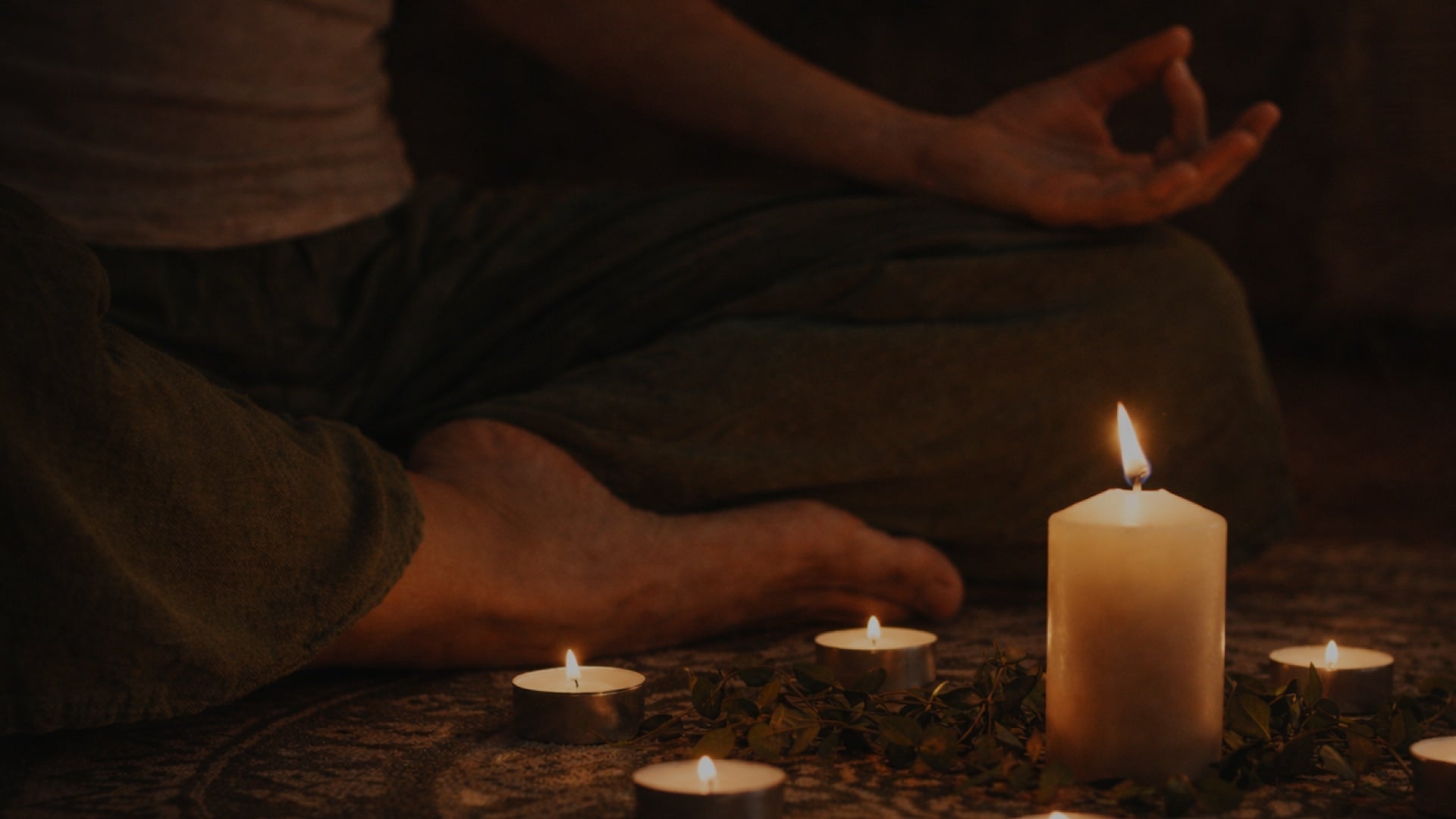 Person meditating with lit candles in a dark setting