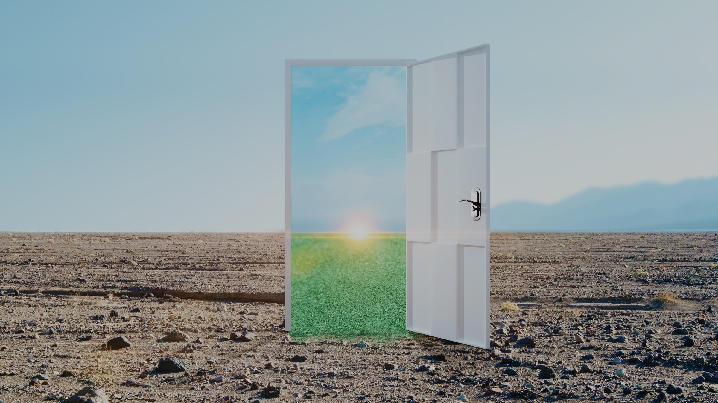 Open door in a desert landscape with a green field and blue sky on the other side.