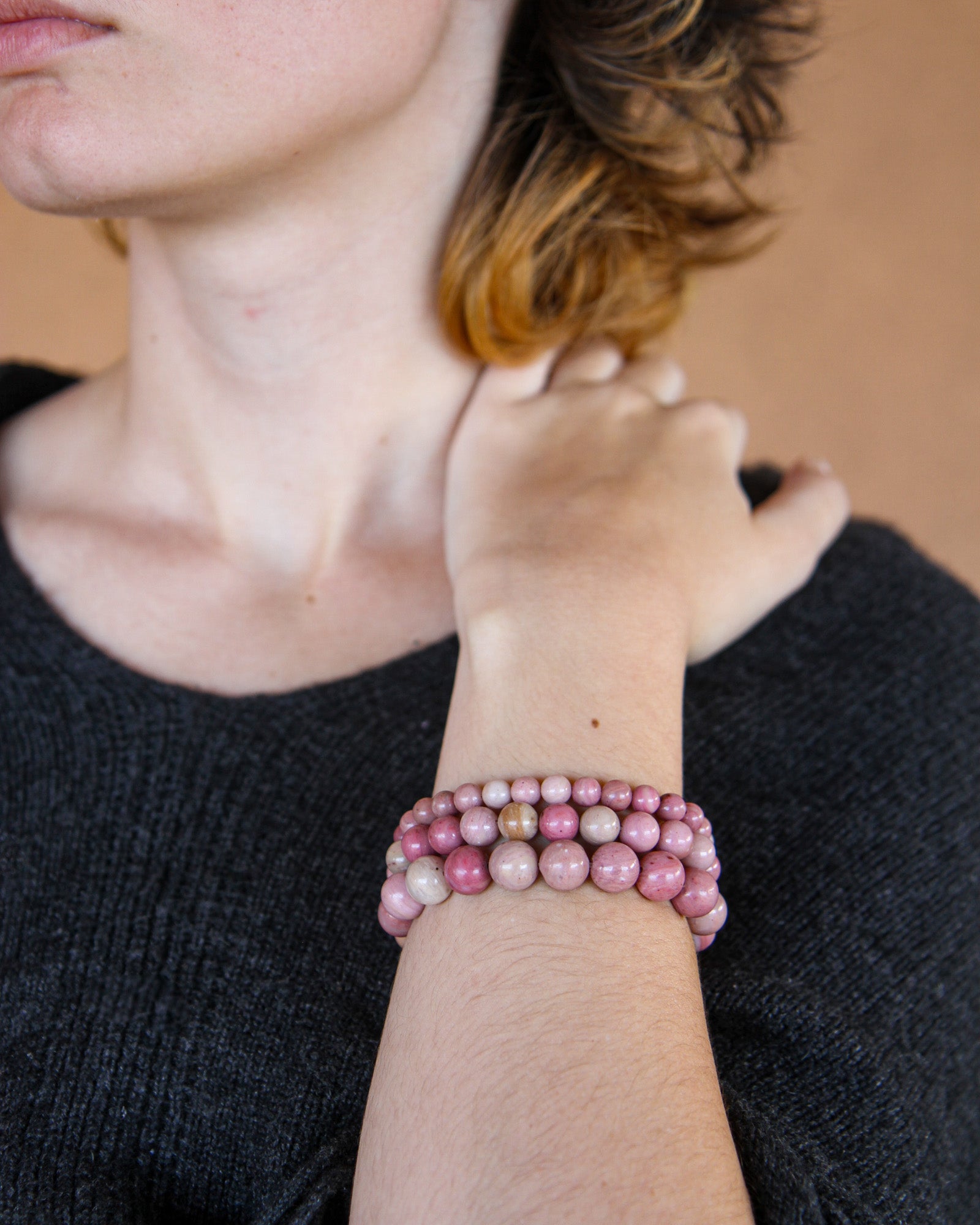 Person wearing a stack of pink beaded bracelets on a neutral background