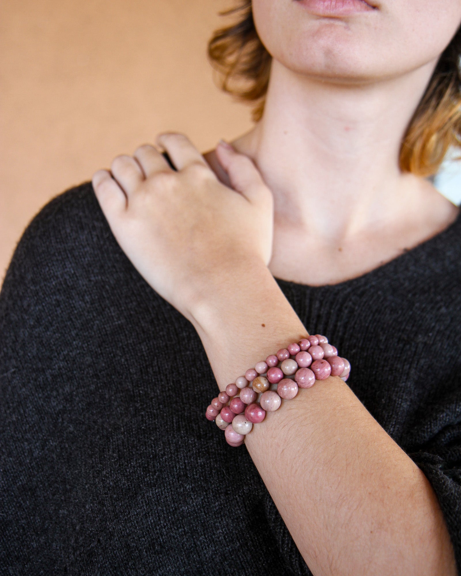 Person wearing a stack of pink beaded bracelets on a plain background