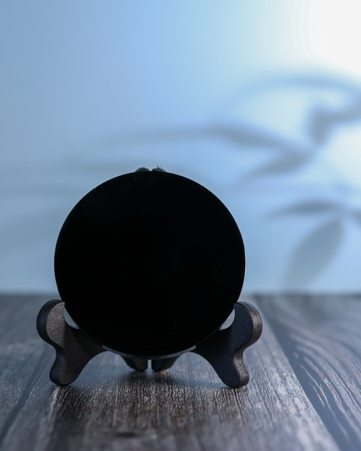 Obsidian scrying mirror on a weathered wood surface in soft daylight