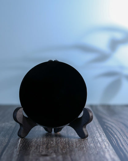 Obsidian scrying mirror on a weathered wood surface in soft daylight