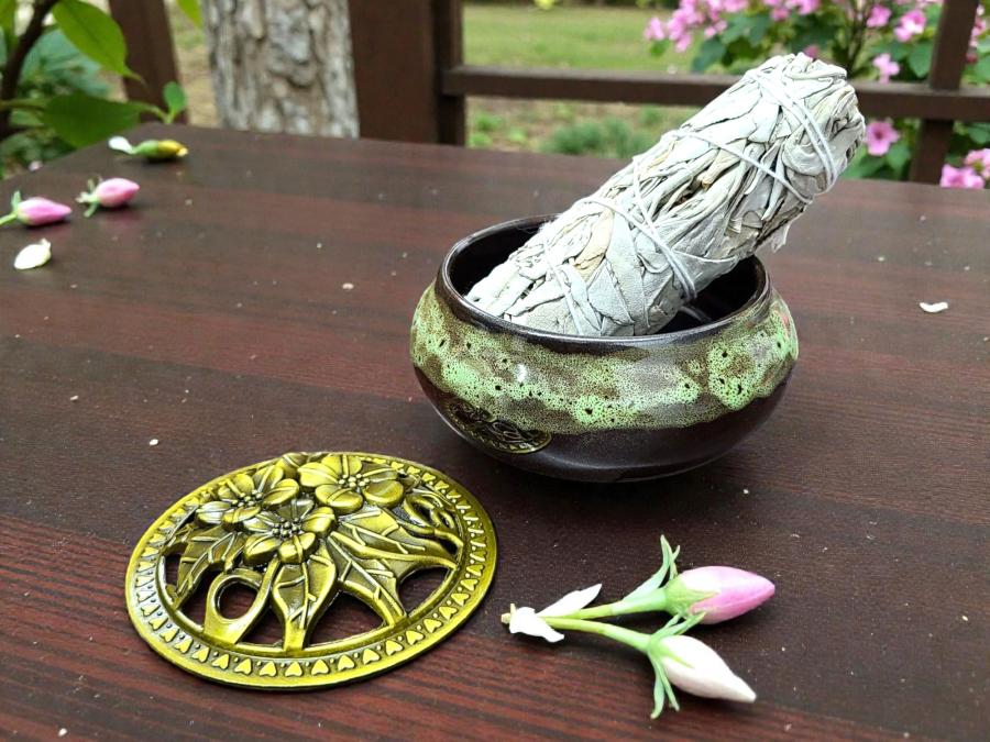 Ceramic burner bowl holding a white sage bundle, with the brass floral lid beside it